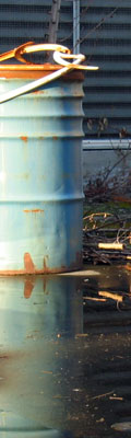 This is a simple picture of a large metal barrel and it's reflection in the puddle of water that it is resting in. The can is blue and rusted orange along the top.